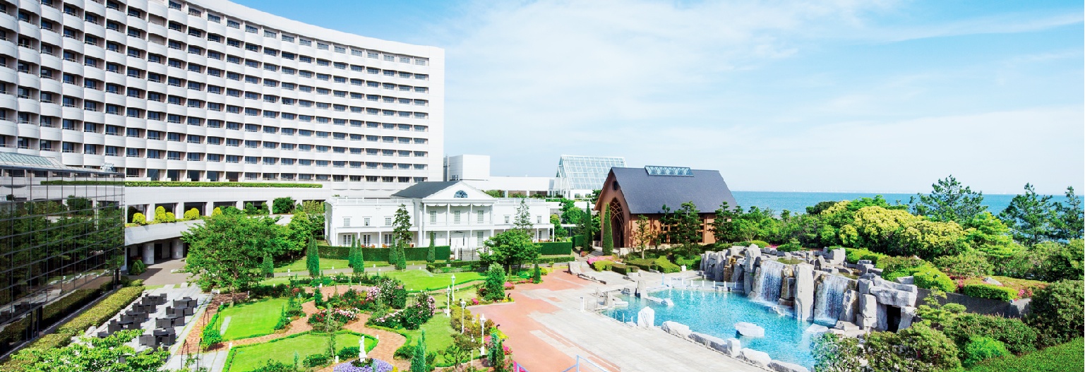 Marriott resort in Japan with a curved building, a white mansion, a chapel, and a landscaped garden featuring a stone waterfall and a blue pool.